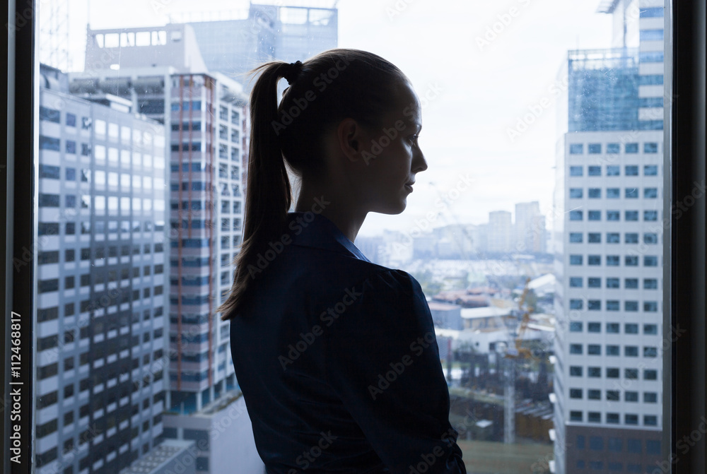Silhouette of thoughtful female looking out her office window. 