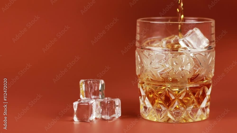 Whiskey being poured into glass with ice cubes Whiskey being poured into glass with ice cubes