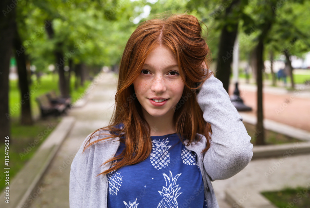 red-haired girl smiling with perfect smile and white teeth in a park and looking at camera