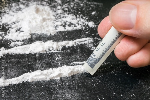 Hand of man holds rolled banknote for snorting cocaine powder.