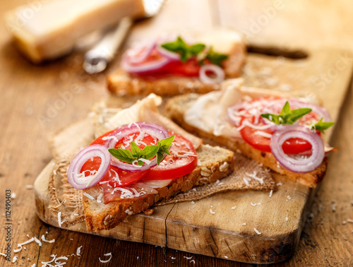 Sandwich with smoked ham, tomato, red onion, grana padano cheese and fresh oregano on a wooden board