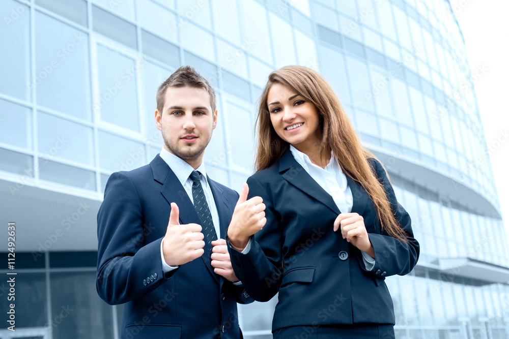 Successful young business people showing thumbs up sign, standin Successful young business people showing thumbs up sign, standin