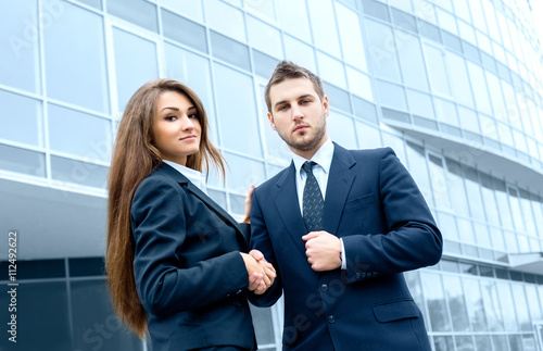 Business partners shake hands, standing in front of his office.