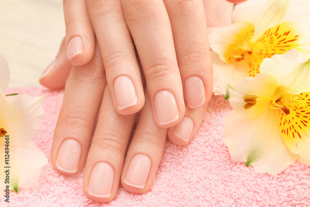 Spa concept. Woman hands with beautiful manicure and flowers on towel, close up