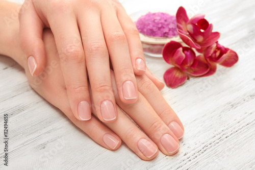 Woman hands with beautiful manicure and purple orchid on wooden background, close up