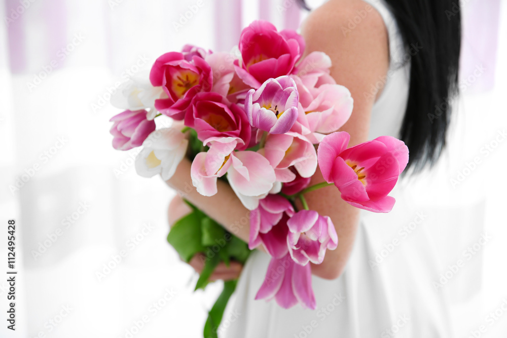 Naklejka premium Young woman holding tulips and standing beside the window