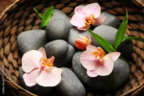 Spa stones and orchid flowers in wicker basket