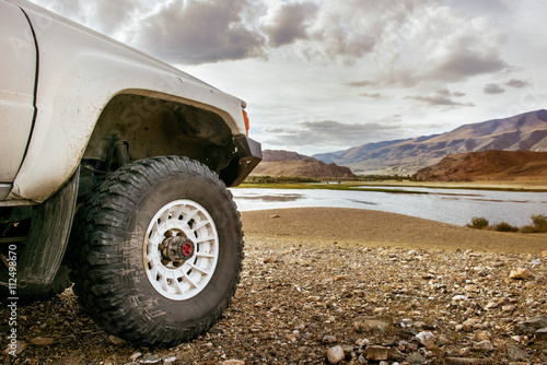 Big SUV car wheel stands on backdrop of mountain lake