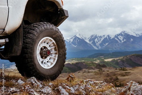 Big car wheel is standing on the rocks on mountain backdrop. Altay mountains, Siberia, Russia