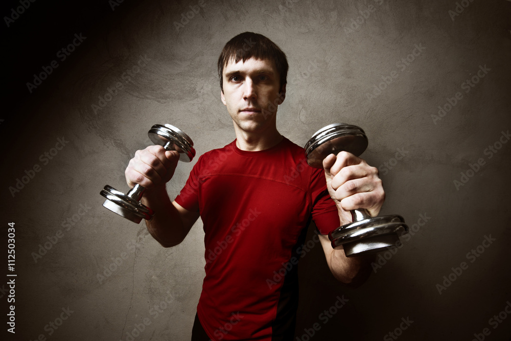 Muscle man posing with dumbbells on gray wall backdrop Muscle man posing with dumbbells on gray wall backdrop