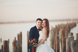 Beautiful young wedding couple, bride and groom posing near wooden poles on the background sea