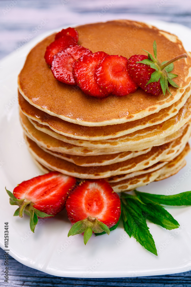 Pancakes with fresh strawberry and mint on white plate on blue wooden background. Closeup. Pancakes with fresh strawberry and mint on white plate on blue wooden background. Closeup.