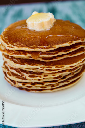Pancakes with butter and honey on white plate on blue wooden background. Stack of wheat golden pancakes or pancake cake, closeup.