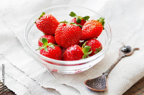 Fresh juicy strawberries in glass bowl. Rustic background with homespun napkin and vintage spoon.