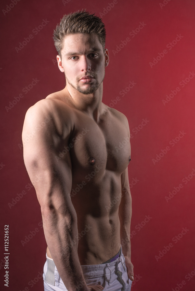 Fototapeta premium Handsome young and attractive man, male model. Shirtless male model against a red background.