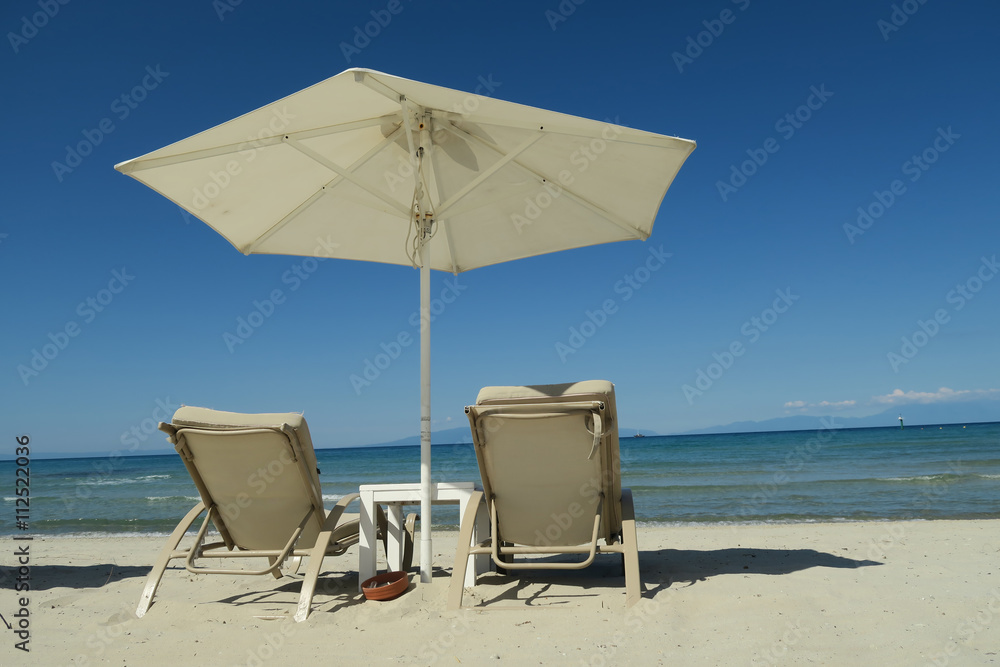 White umbrella with empty beach beds on Greece. Sunbeds with deckchairs on a summer beach at Halkidiki, Greece.