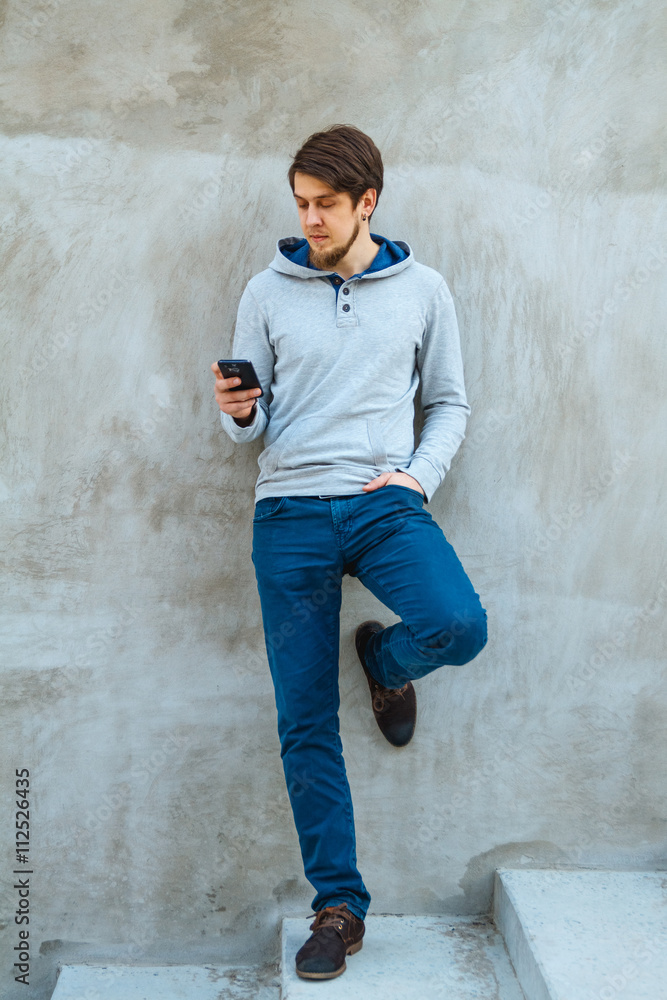 Obraz premium Young man writing sms standing by concrete wall. copy space