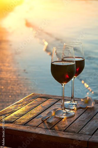Romantic beach scene: two glasses of red wine at sunset near water