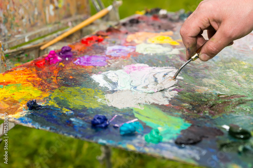 Hand of a male artist mixing white paint on an old palette outdo