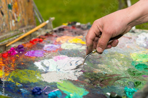 Hand of a male painter mixing colors on an old palette outdoors