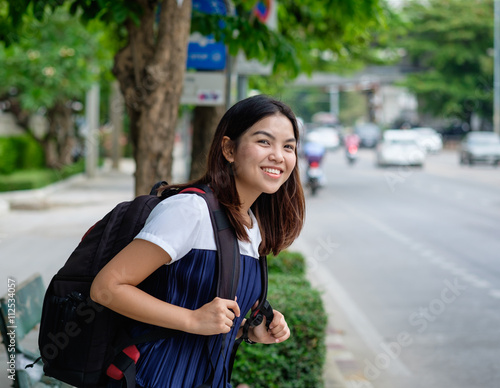 Young woman standing at bus stop on street city. Asian woman waiting for bus. Woman student in private dress standing at bus stop. Public transport stop in Thailand. bus stop on street in asian.
