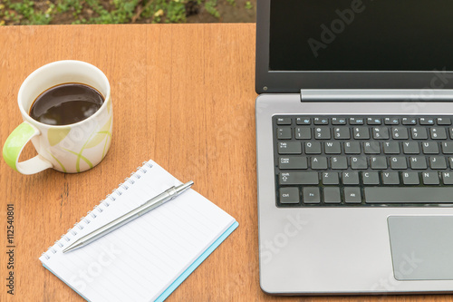 Cup of coffee with a laptop and a notebook on a wooden table.