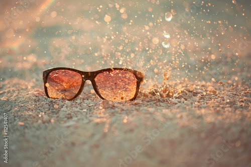 yellow sunglasseson sandy beach with splash