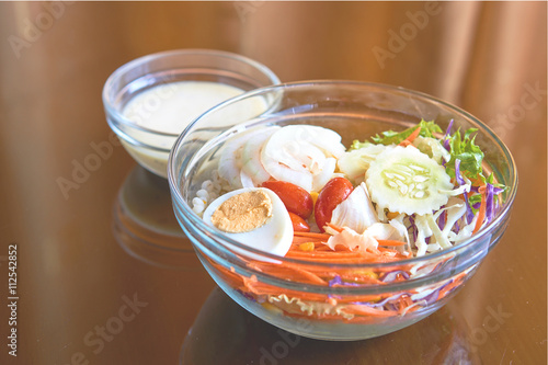 Mixed vegetables and egg salads in a glass transparent bowl on orange curtain background with reflection