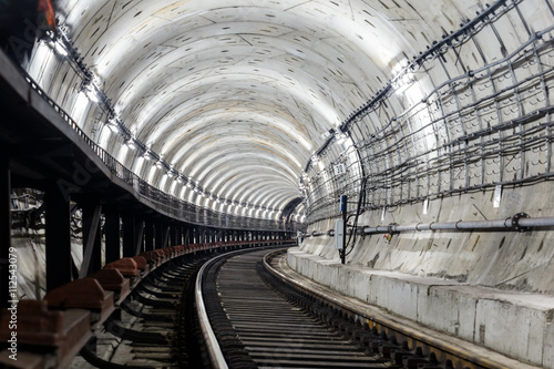 circular tunnel subway with rails and sleepers turns right and is illuminated with white light.