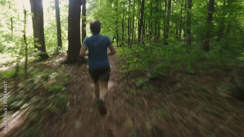 Adult man running jogging outdoors in a forest nature on a forest trail and enjoying it and looking happy Adult man running jogging outdoors in a forest nature on a forest trail and enjoying it and looking happy