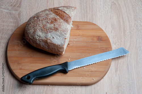 Cutting board, bread and a knife lying on a wooden table
