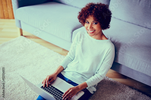 Happy young african woman with laptop sitting in living room photo