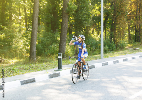 Thirst. Female cyclist drinks water near bike