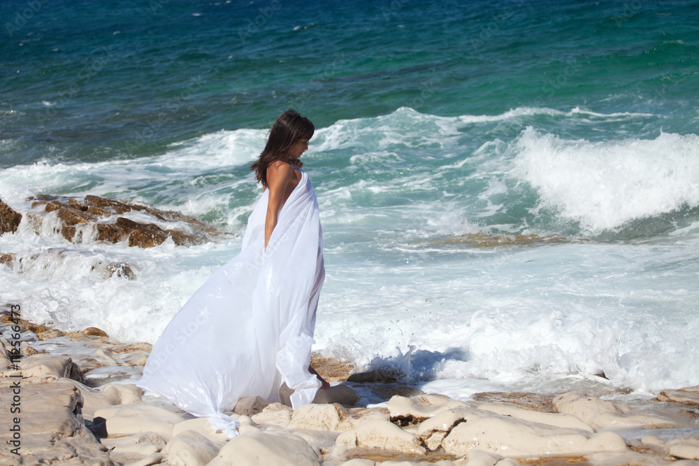 Woman in white cape dress enjoys on the rocky beach on the sea Woman in white cape dress enjoys on the rocky beach on the sea