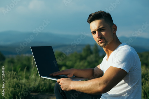 Pensive muscular man with laptop outdoor