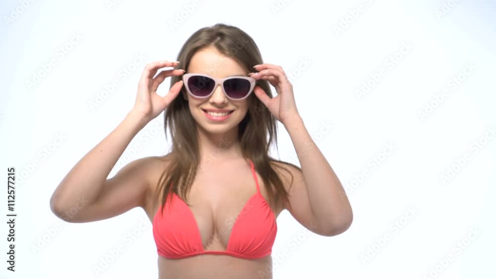 Happy young brunette woman wearing pink bikini and putting on and off her sunglasses on white background in slowmotion Happy young brunette woman wearing pink bikini and putting on and off her sunglasses on white background in slowmotion