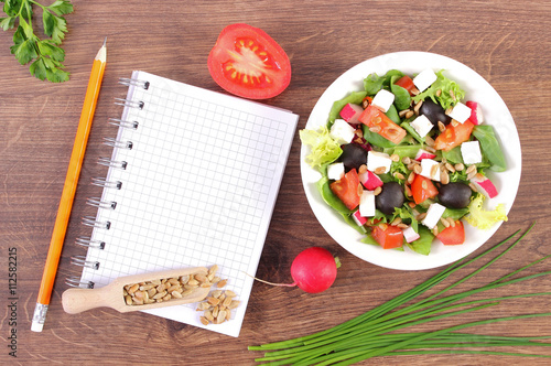 Fresh greek salad with vegetables and notepad for writing notes, healthy nutrition