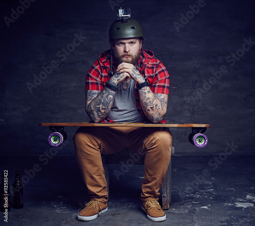 Male in red shirt posing with longboard in studio.