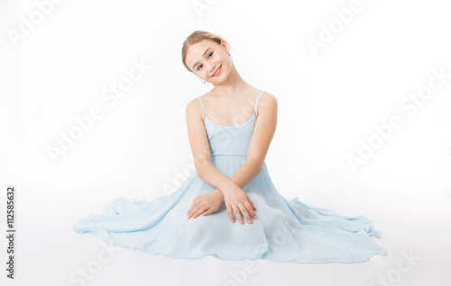 Happy little girl in a blue dress is sitting on the floor on a white background