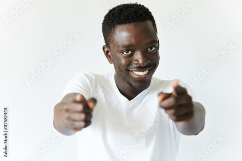 Handsome happy young African student looking with ultrawhite smile at the camera after doing a great job at university, pointing a finger at the viewer. Success and achievement concept. Film effect