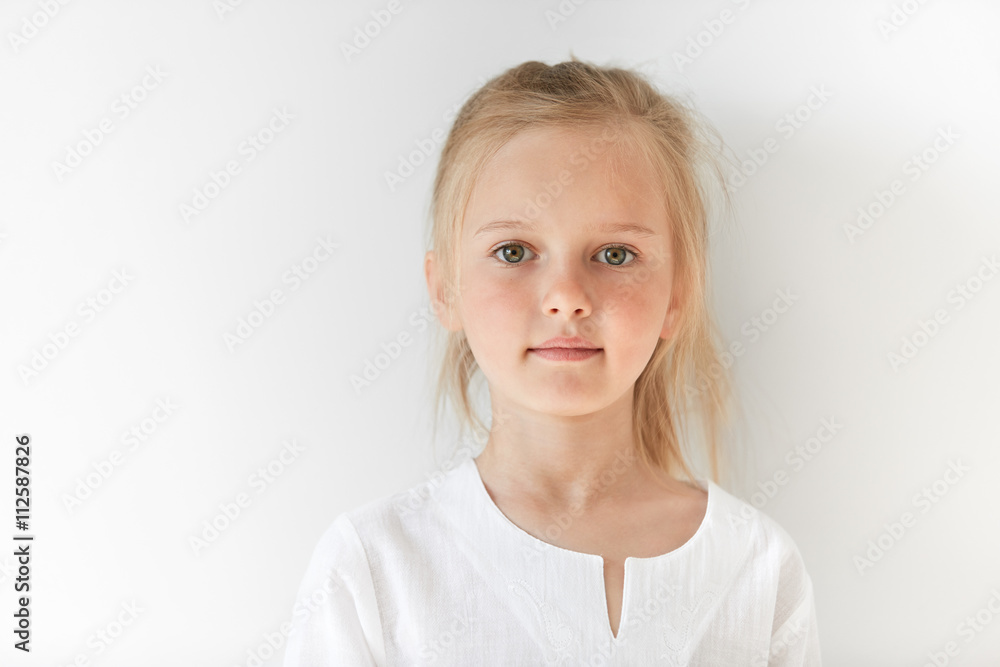 Portrait of angel-like child in white morning light in studio. Little European girl with blond hair looking attractive and balanced showing neutral emotions and radiating tranquility. Portrait of angel-like child in white morning light in studio. Little European girl with blond hair looking attractive and balanced showing neutral emotions and radiating tranquility.