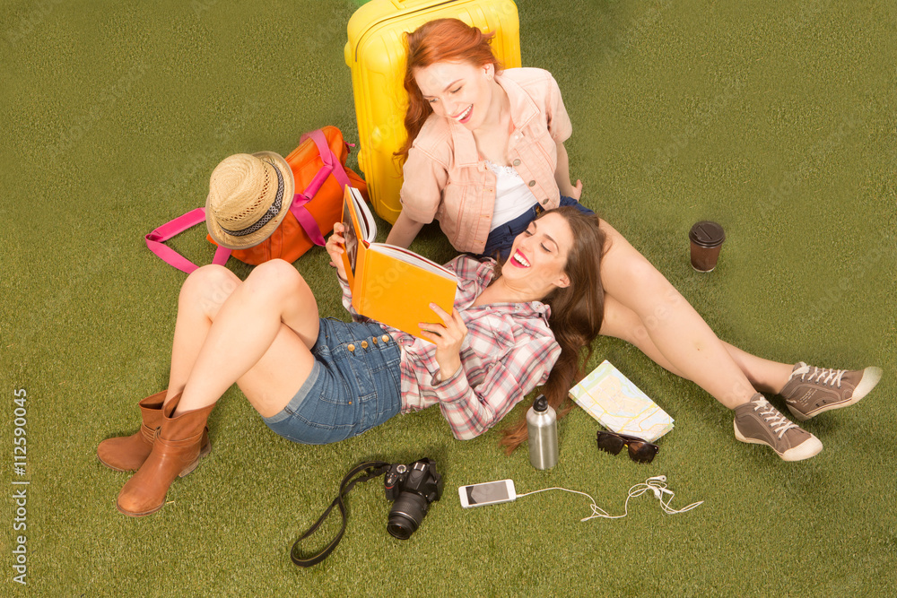 Naklejka premium Top view of cheerful beautiful tourist lady lying on green grass, communicating about places of sightseeing and looking at notebook.