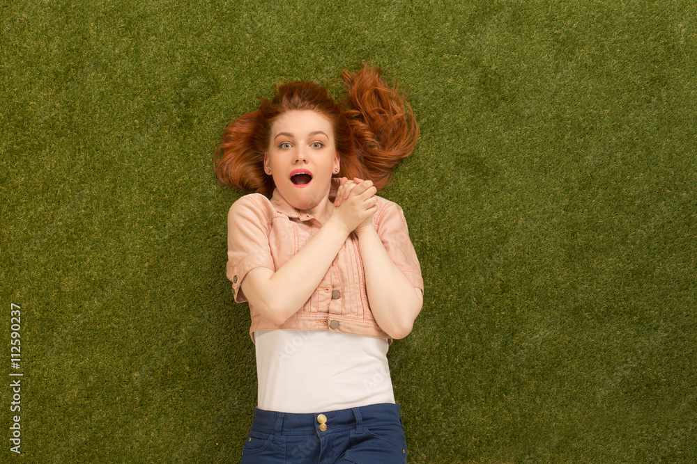 Picture of amazed or excited beautiful woman lying on green grass. Happy woman looking at camera and expressing emotions. Picture of amazed or excited beautiful woman lying on green grass. Happy woman looking at camera and expressing emotions.