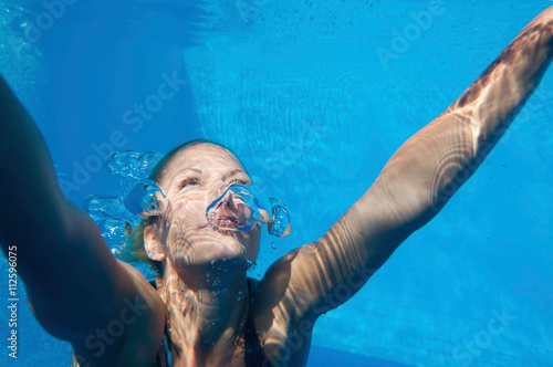 Fotografie Swimming up, underwater shot of a young woman swimming towards the surface
