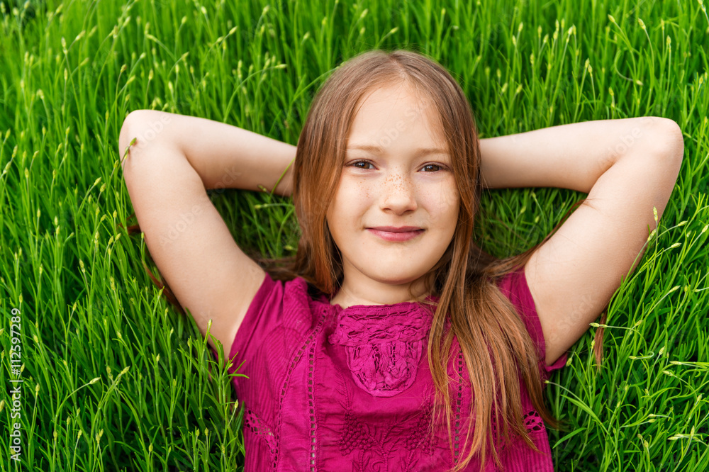 Young little girl resting outdoors. Close up outdoor portrait of adorable little girl of 8-9 years old laying on fresh lavender grass Young little girl resting outdoors. Close up outdoor portrait of adorable little girl of 8-9 years old laying on fresh lavender grass