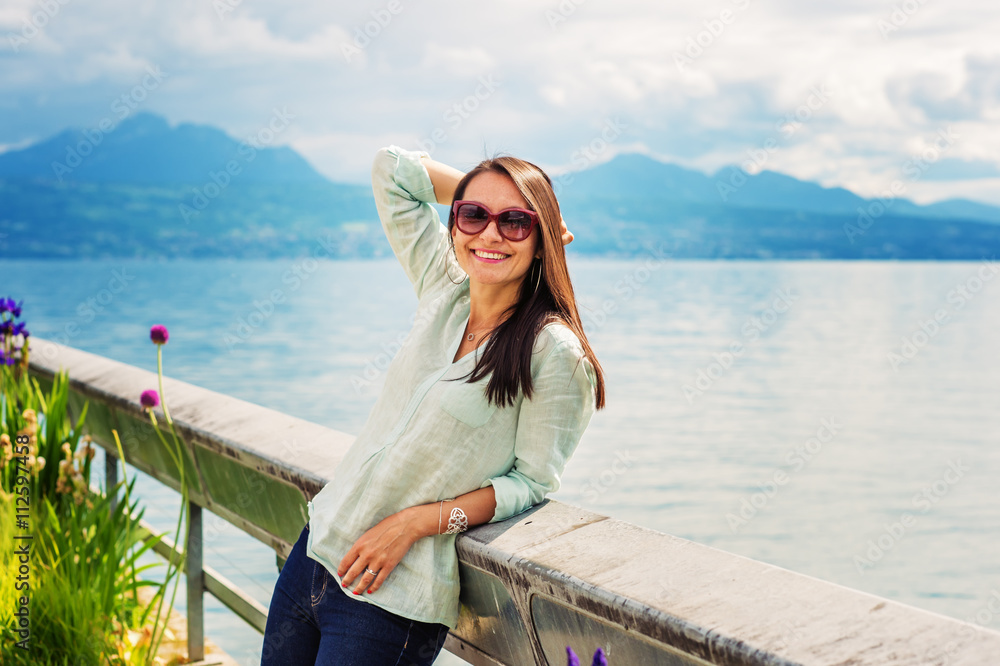 Portrait of young brunette woman resting outdoors by the lake, wearing sunglasses. Image taken on lake Geneva, Switzerland Portrait of young brunette woman resting outdoors by the lake, wearing sunglasses. Image taken on lake Geneva, Switzerland
