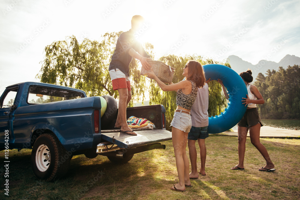 Young friends unloading pickup truck on camping trip - obrazy, fototapety, plakaty 