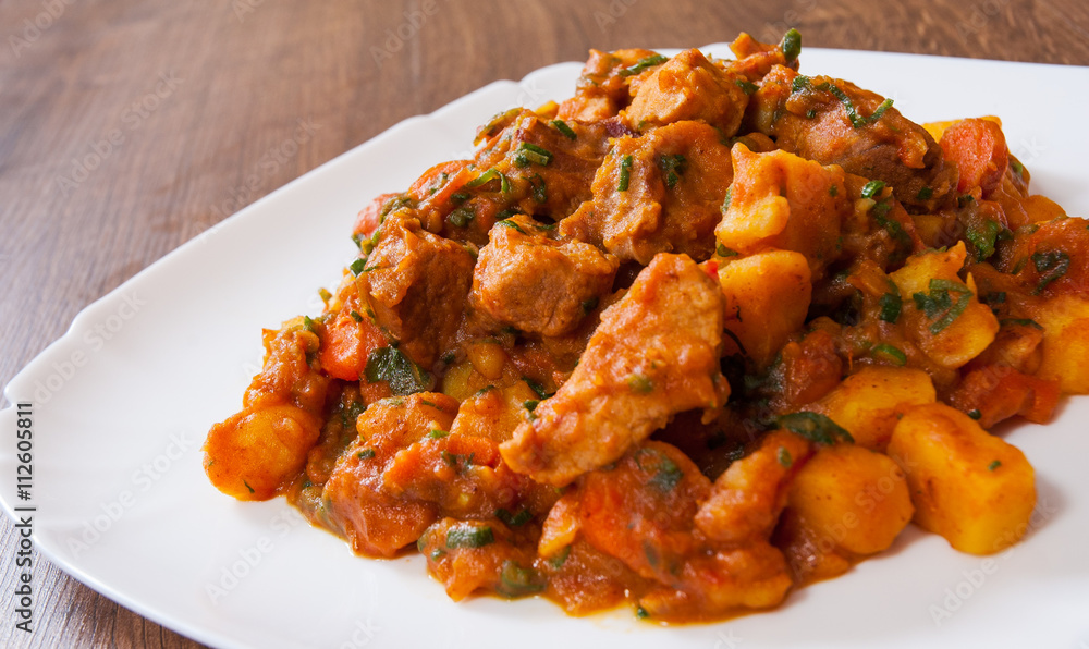 Stewed meat with vegetables in a plate on wooden table Stewed meat with vegetables in a plate on wooden table