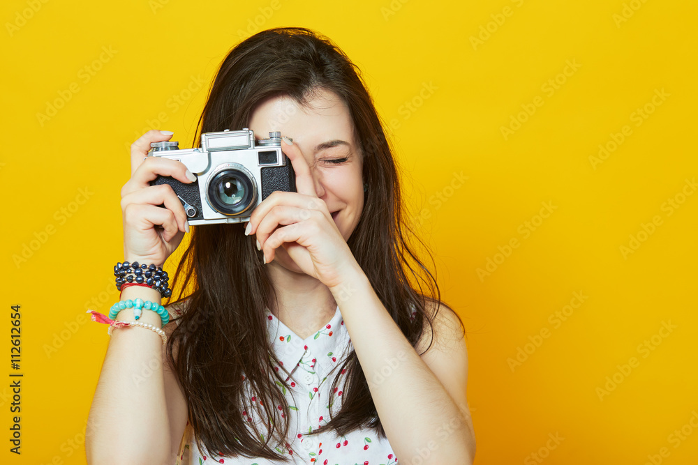 young girl with retro camera smiling against a yellow wall