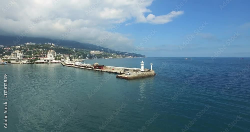 Aerial shot of the white lighthouse on the pier with resort town Crimea on the background. Shoot is made on the peninsula of Crimea Aerial shot of the white lighthouse on the pier with resort town Crimea on the background. Shoot is made on the peninsula of Crimea